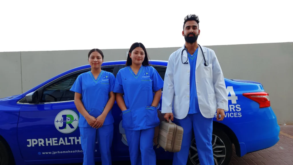 Two female nurses and and a doctor standing in front of a JPR Home Healthcare vehicle in Dubai.