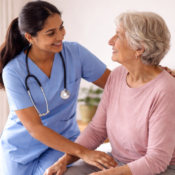 Young Nepali female nurse assisting a senior British woman to sit on the edge of the bed, demonstrating safe bed mobility care for elderly patients at home.