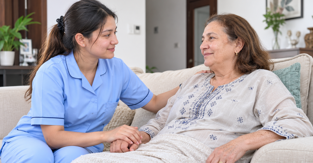 Young female Nepali nurse in a light blue uniform providing compassionate home nursing care to a 69-year-old Moroccan woman in a comfortable UAE home.